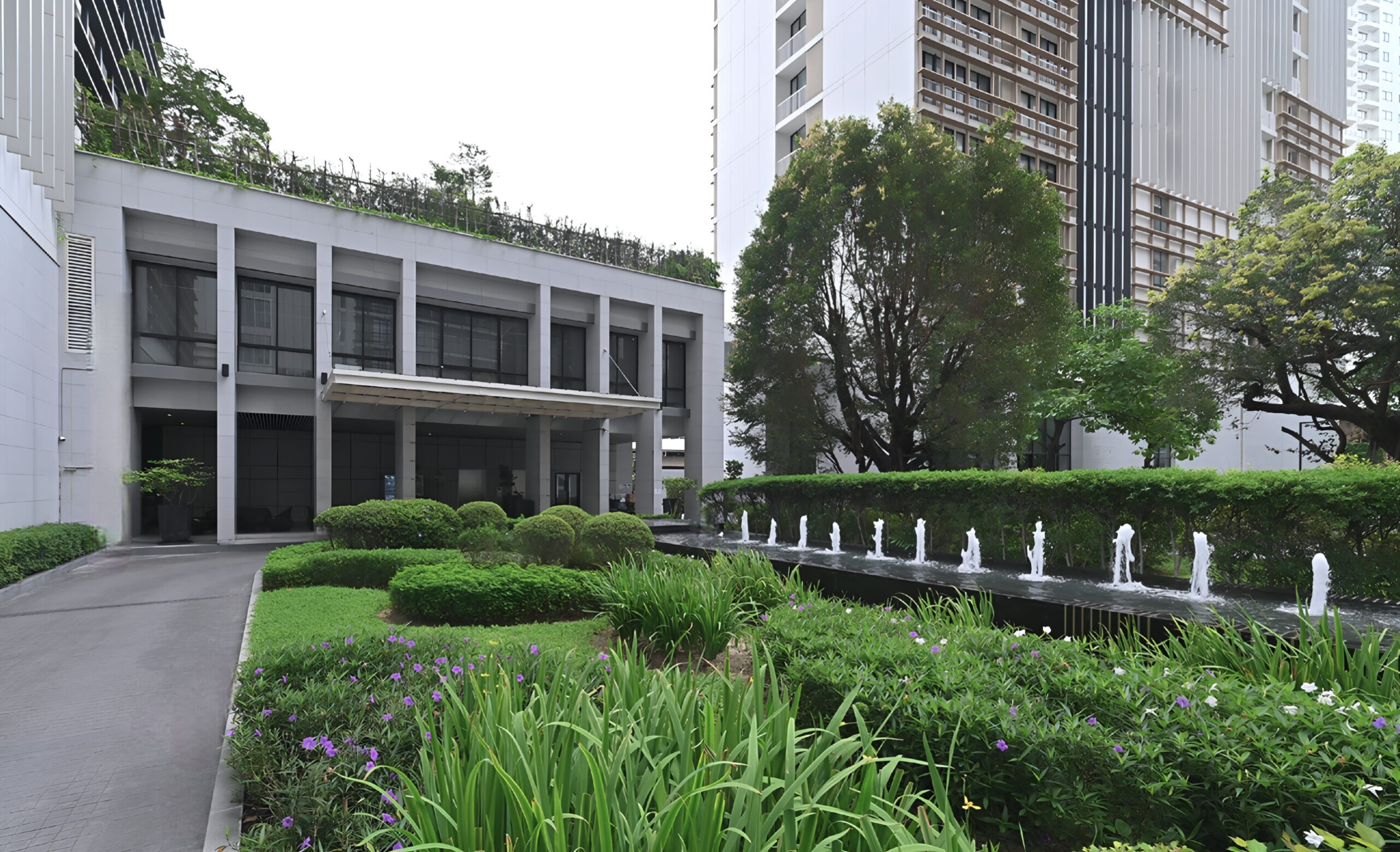 Luxury condominium garden with modern architecture, lush greenery, and a water fountain feature at Park 24 in Bangkok.